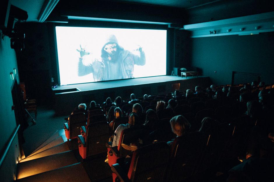 Sala de cine oscura llena de espectadores viendo una película de terror en pantalla grande