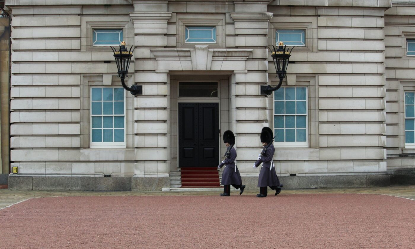 Dos guardias reales con uniforme tradicional marchando frente al Palacio de Buckingham, imagen ilustrativa de la serie sobre Diana