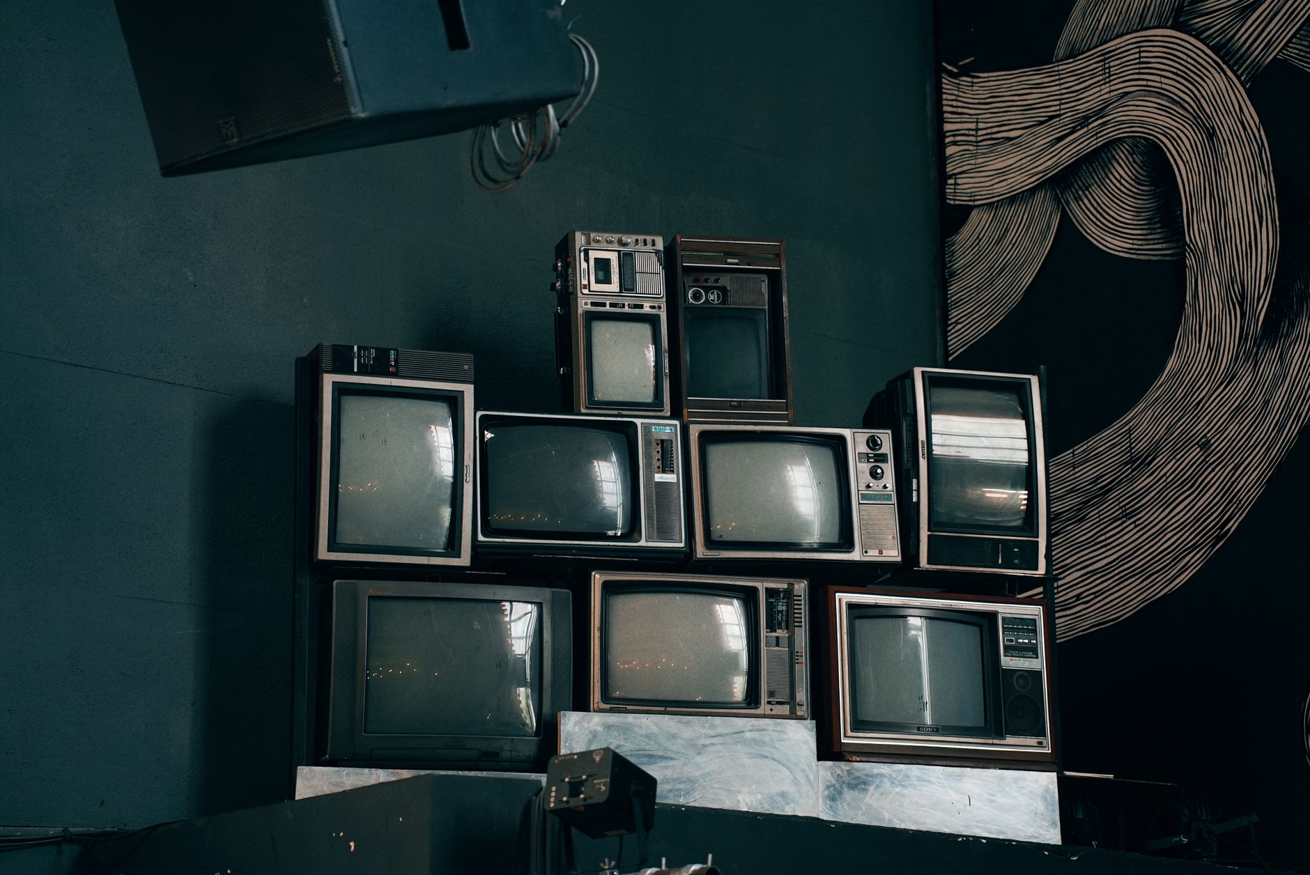 Pila de televisores antiguos en una sala con poca luz, imagen ilustrativa de la serie de terror de televisión