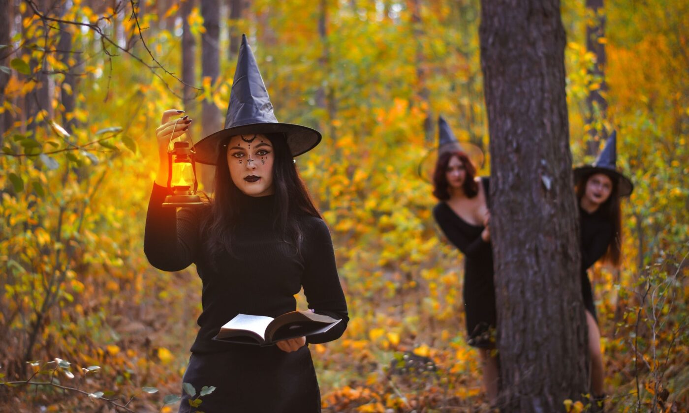 Tres brujas en un bosque otoñal con una linterna, imagen ilustrativa del Coven de American Horror Story