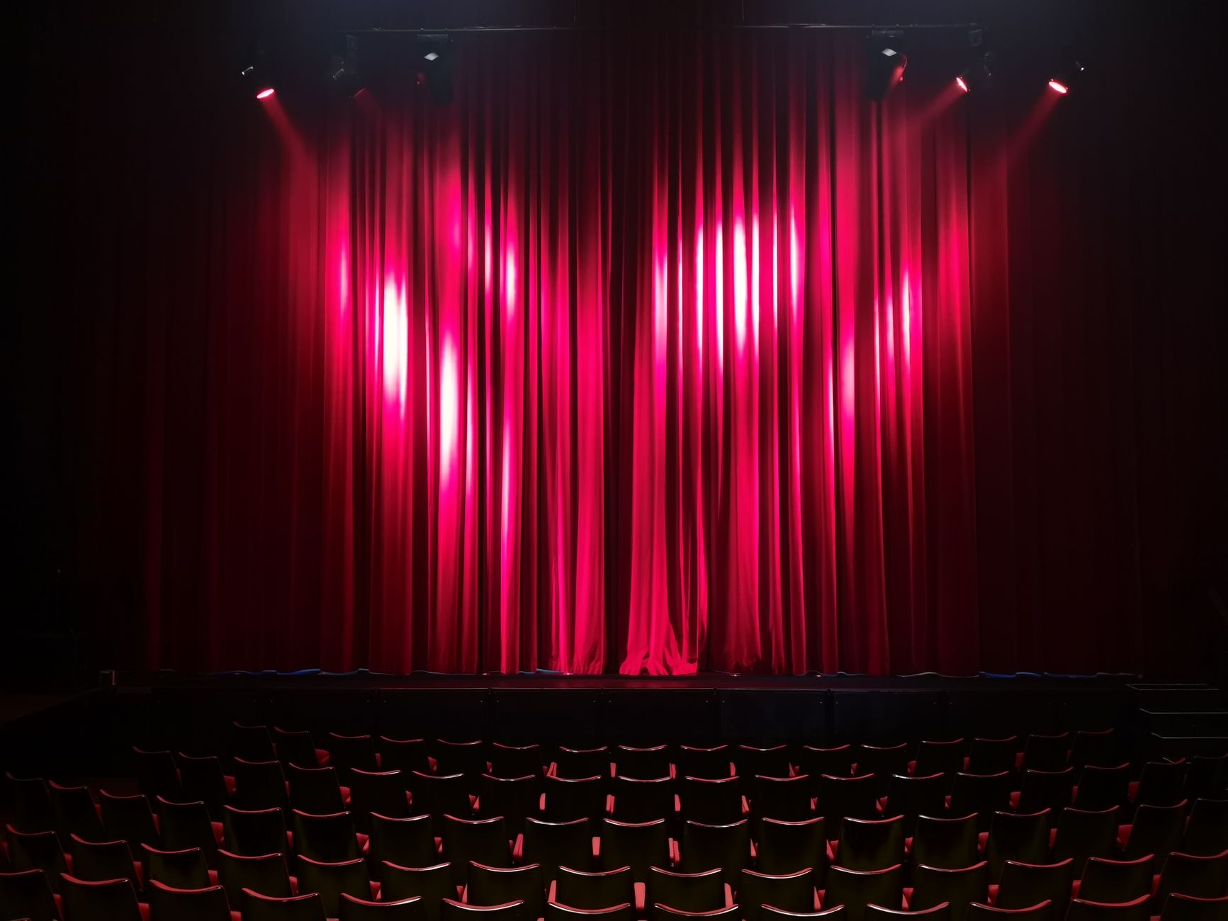 Escenario de teatro vacío con cortinas rojas y butacas, listo para una función de Broadway